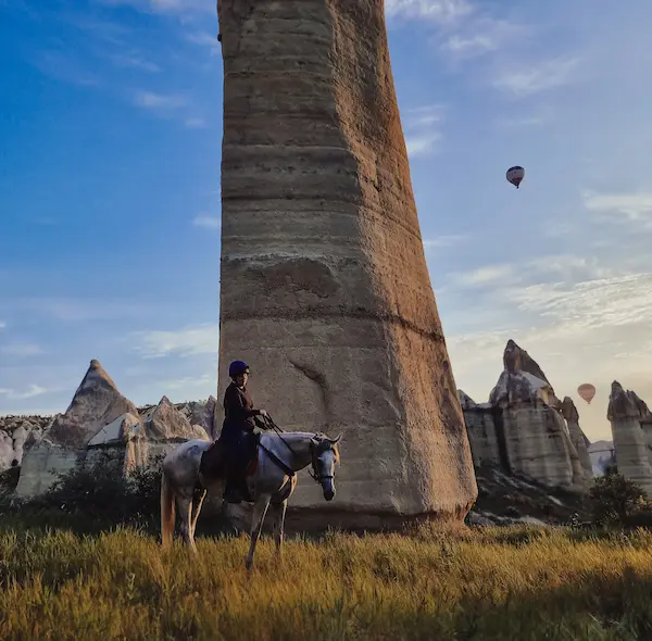 Horseback riding at sunrise in Cappadocia with balloons over the valleys